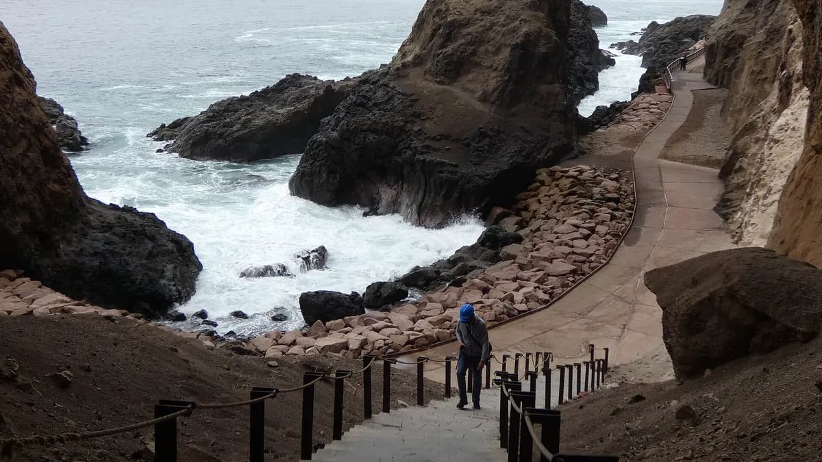Sendero costero con barandas entre rocas y olas en las cuevas de Anzota, al sur de Arica