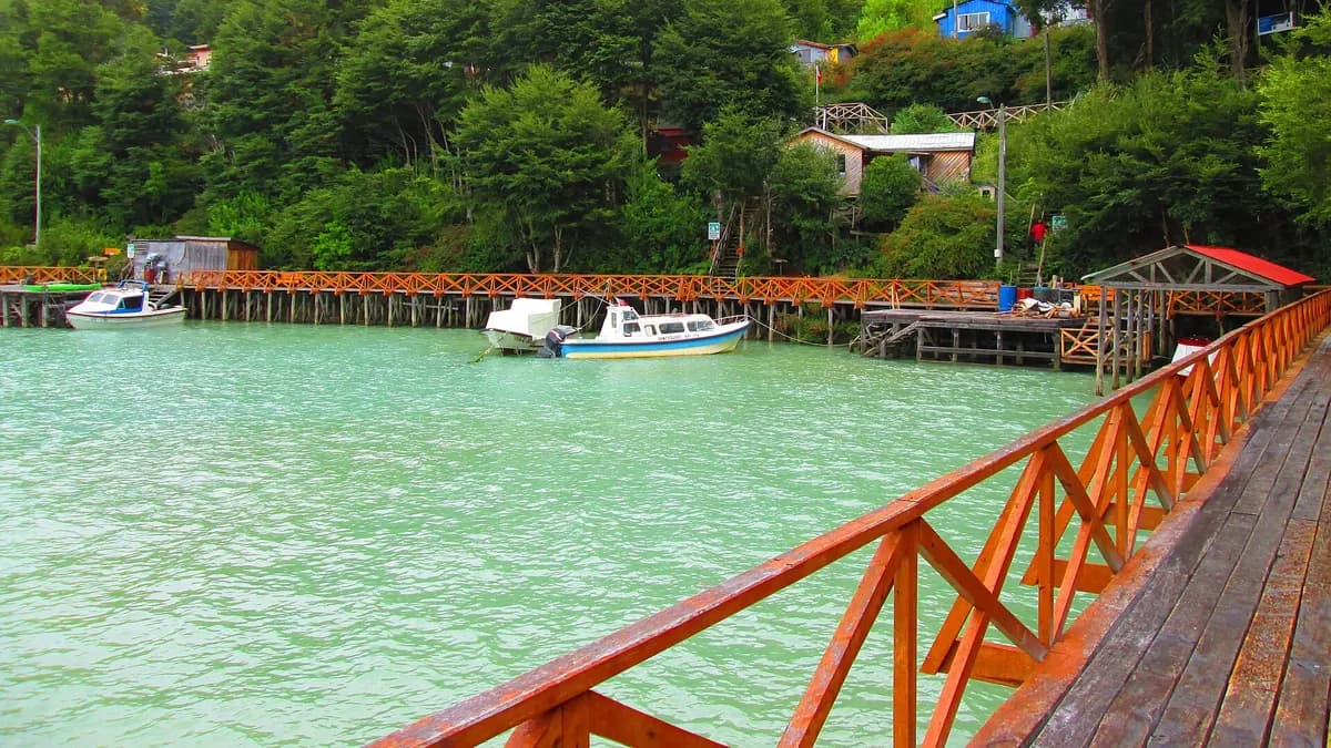 Pasarela de madera roja junto al agua turquesa con botes amarrados en Caleta Tortel