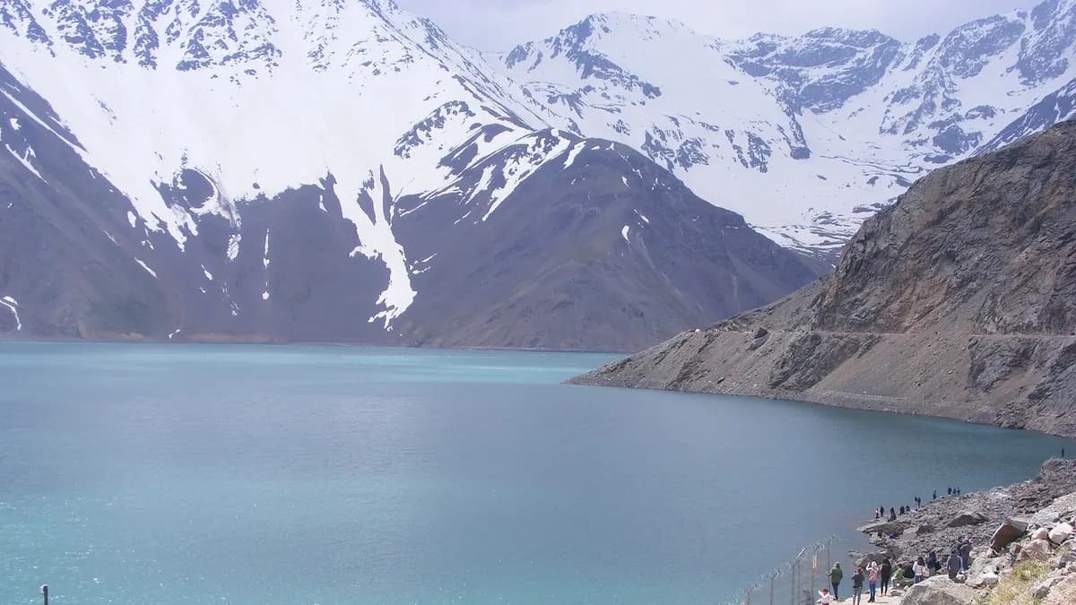 Visiteurs regardant l'Embalse El Yeso depuis la rive, avec des montagnes enneigées au fond