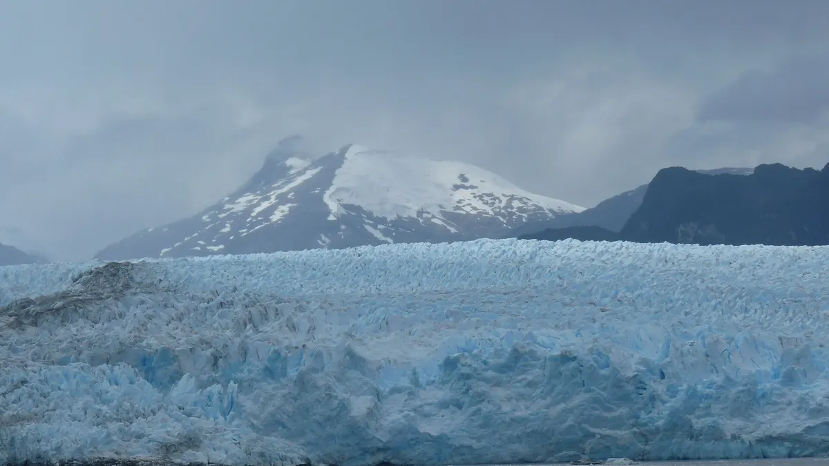 Frente del glaciar Pío XI con paredes de hielo azul y una montaña nevada detrás