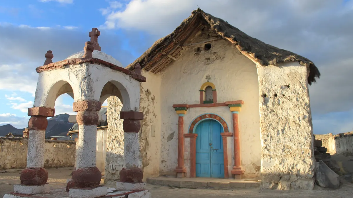 Iglesia de adobe blanqueada con techo de paja y campanario en el pueblo de Parinacota