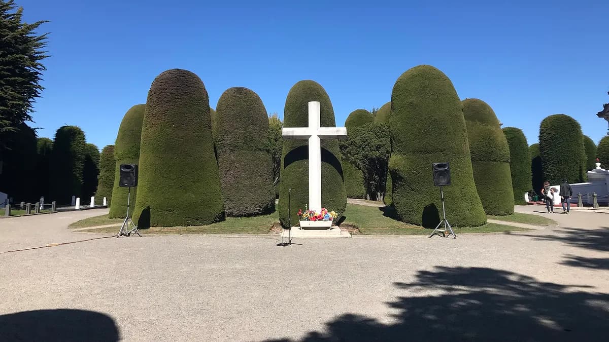 Cipreses recortados y una cruz blanca en la entrada del cementerio municipal de Punta Arenas