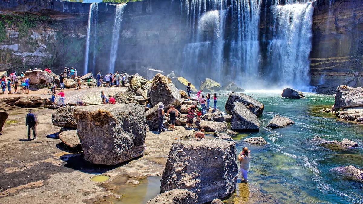 Visitantes sobre las rocas frente a la cortina de agua de los Saltos del Laja