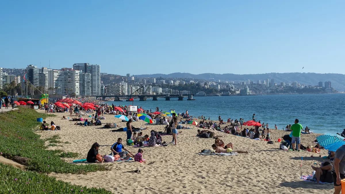 Bañistas en la arena de una playa de Viña del Mar con edificios en la costa